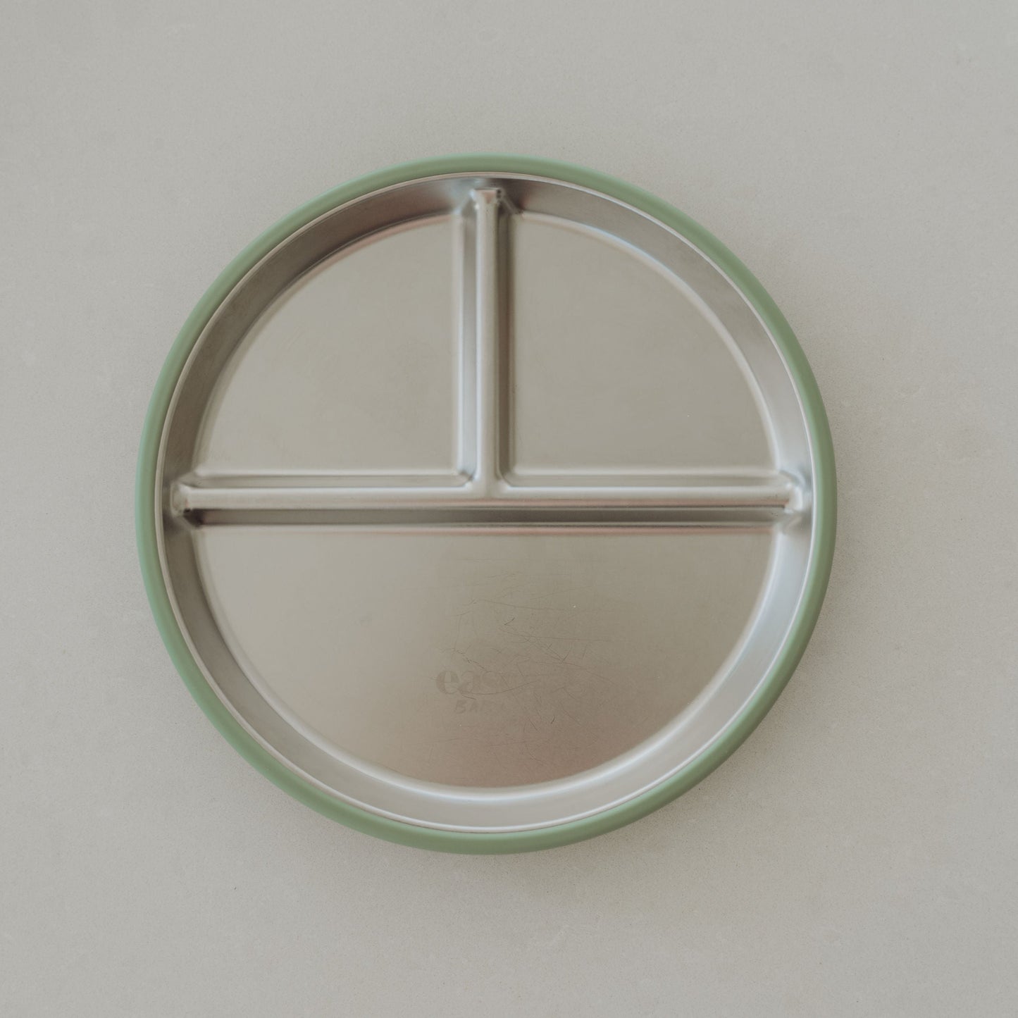 Round stainless steel plate with a green rim on a light gray background