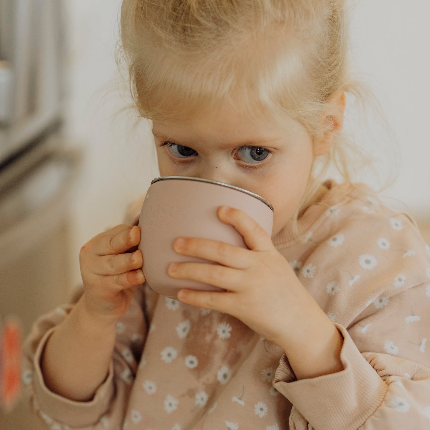 Young girl drinking from a pink cup indoors