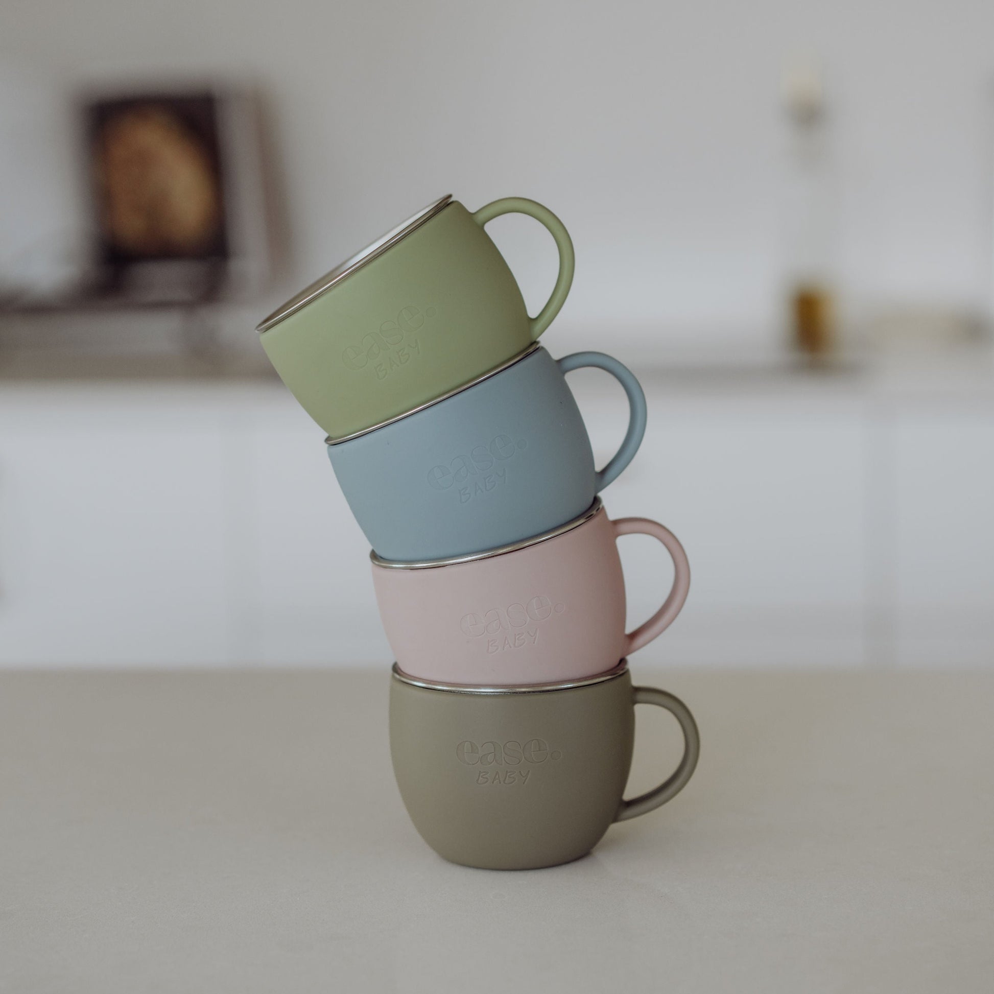 Stack of four stainless steel mugs in pastel colors on a neutral surface.