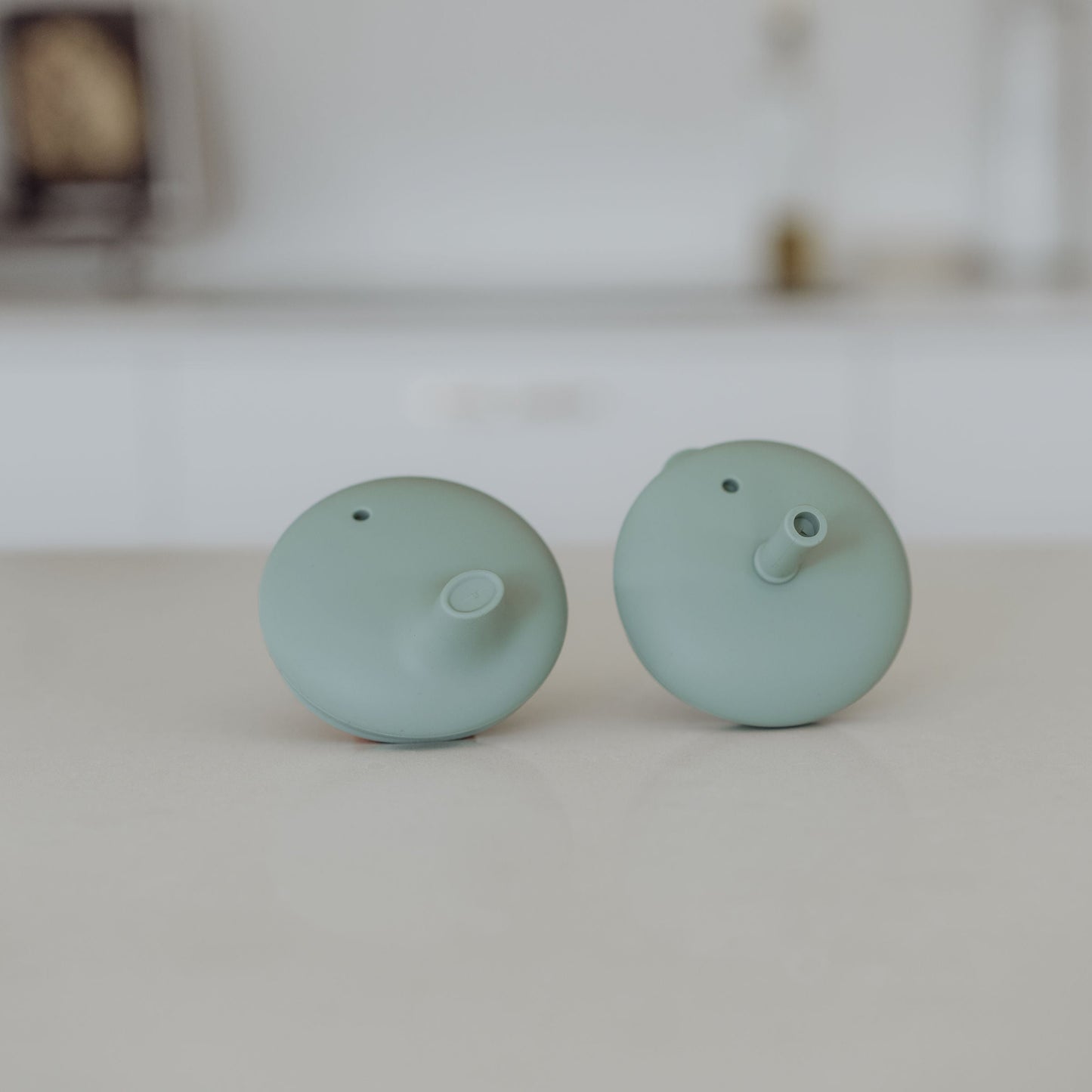 Pair of light green silicone lids on a white surface with a blurred background