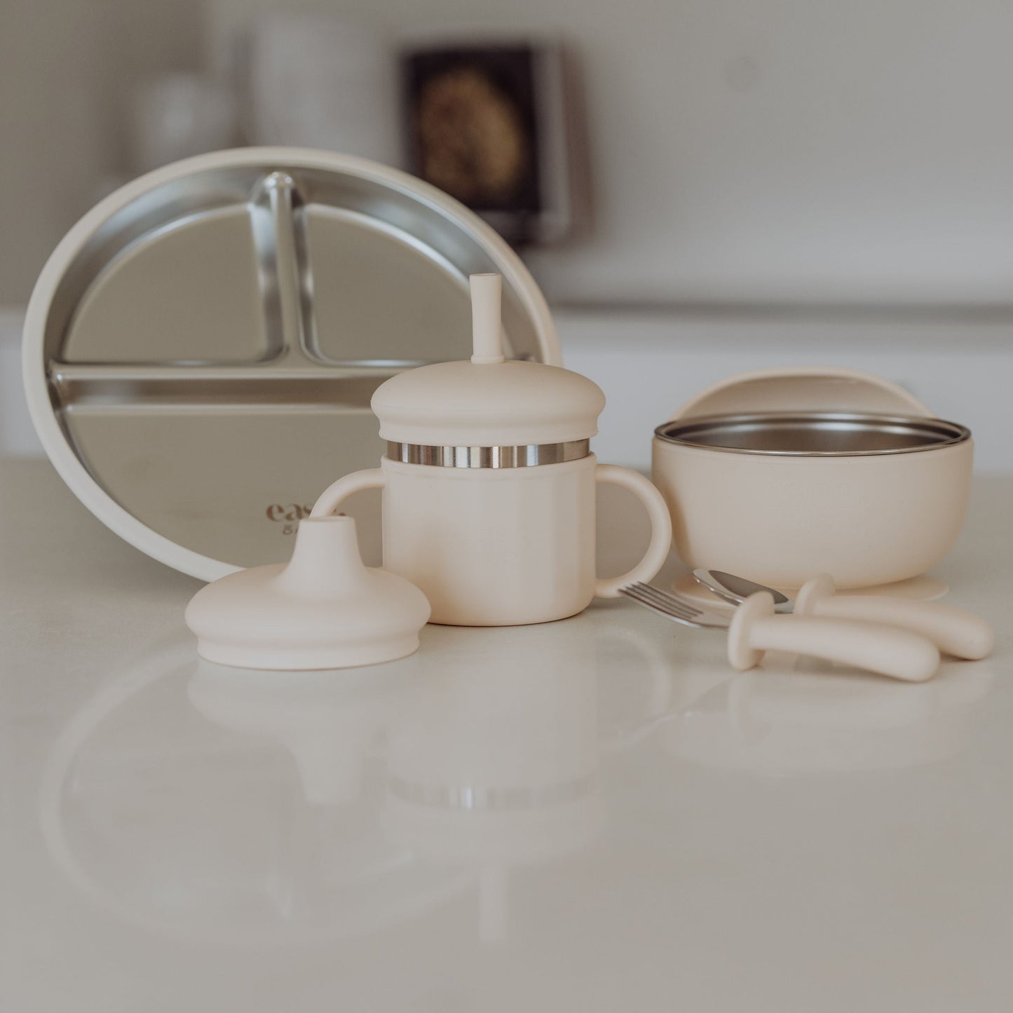 Baby feeding set including a bottle, bowl, and spoon on a white surface.