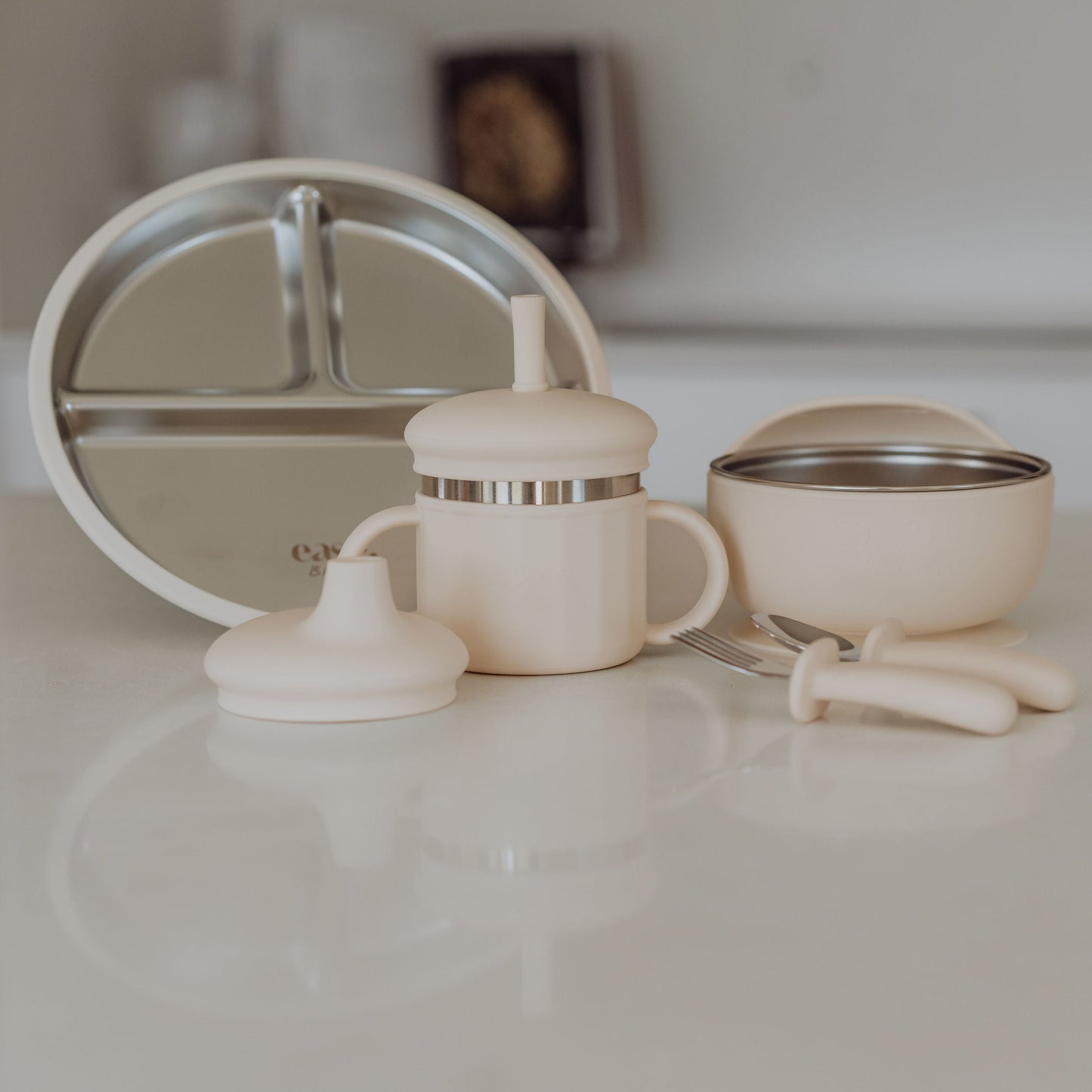 Baby feeding set including a bottle, bowl, and spoon on a white surface.